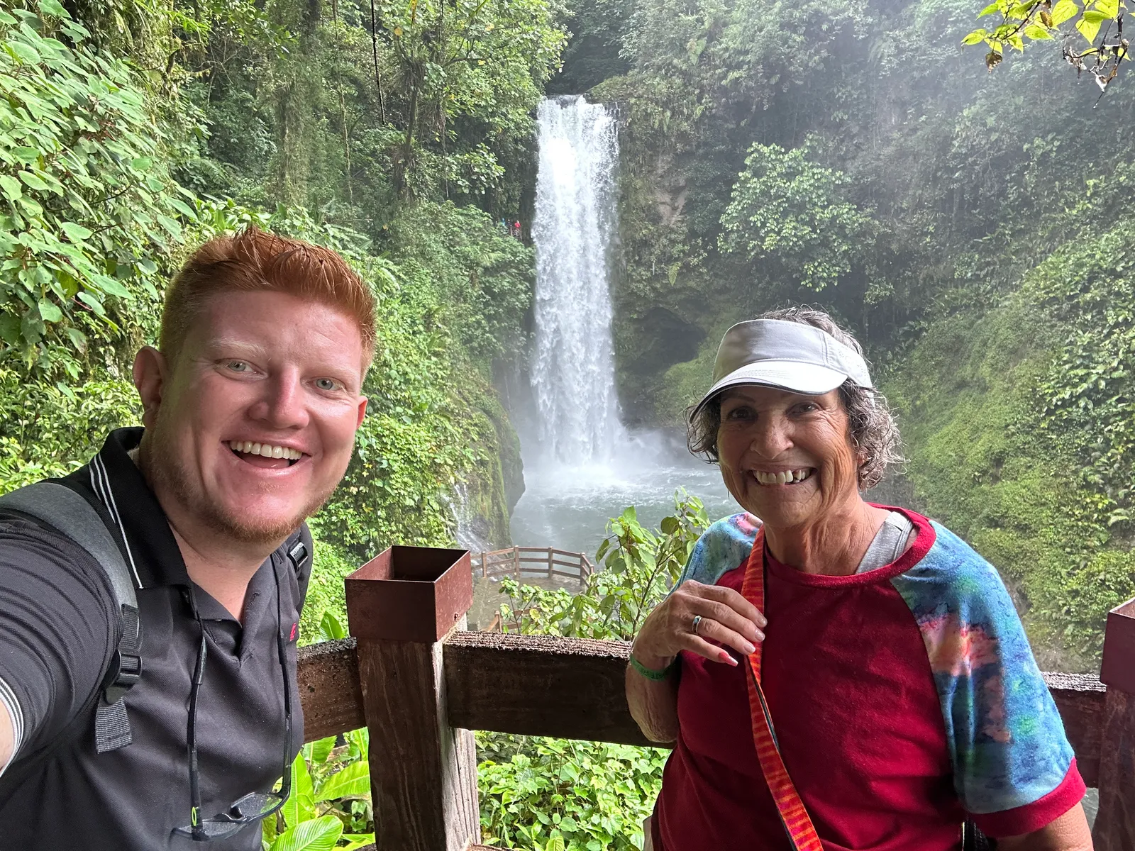 A man and a woman take a selfie on a viewing deck with a waterfall behind.